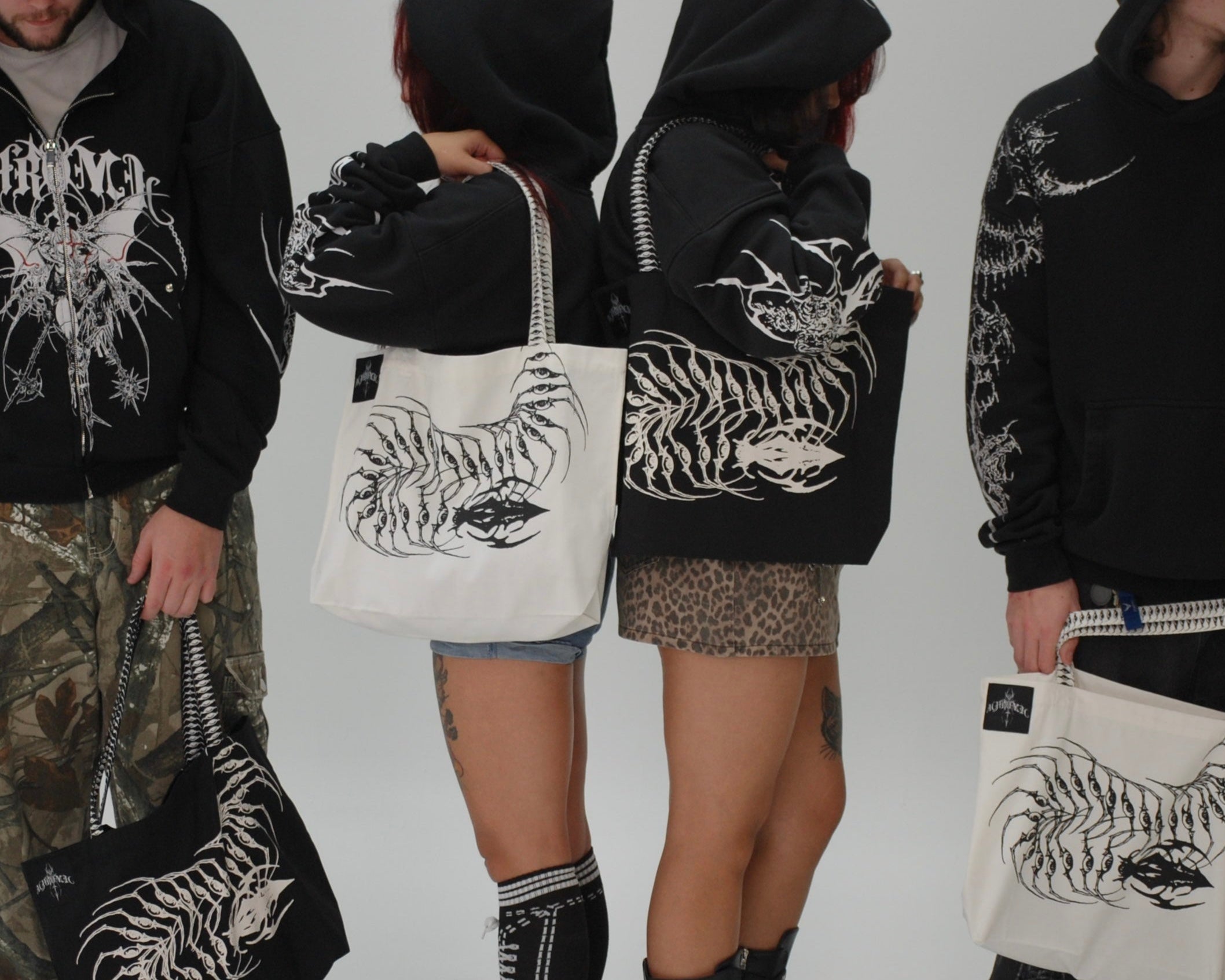 Four people wearing black hoodies with white designs, holding bags with similar designs.